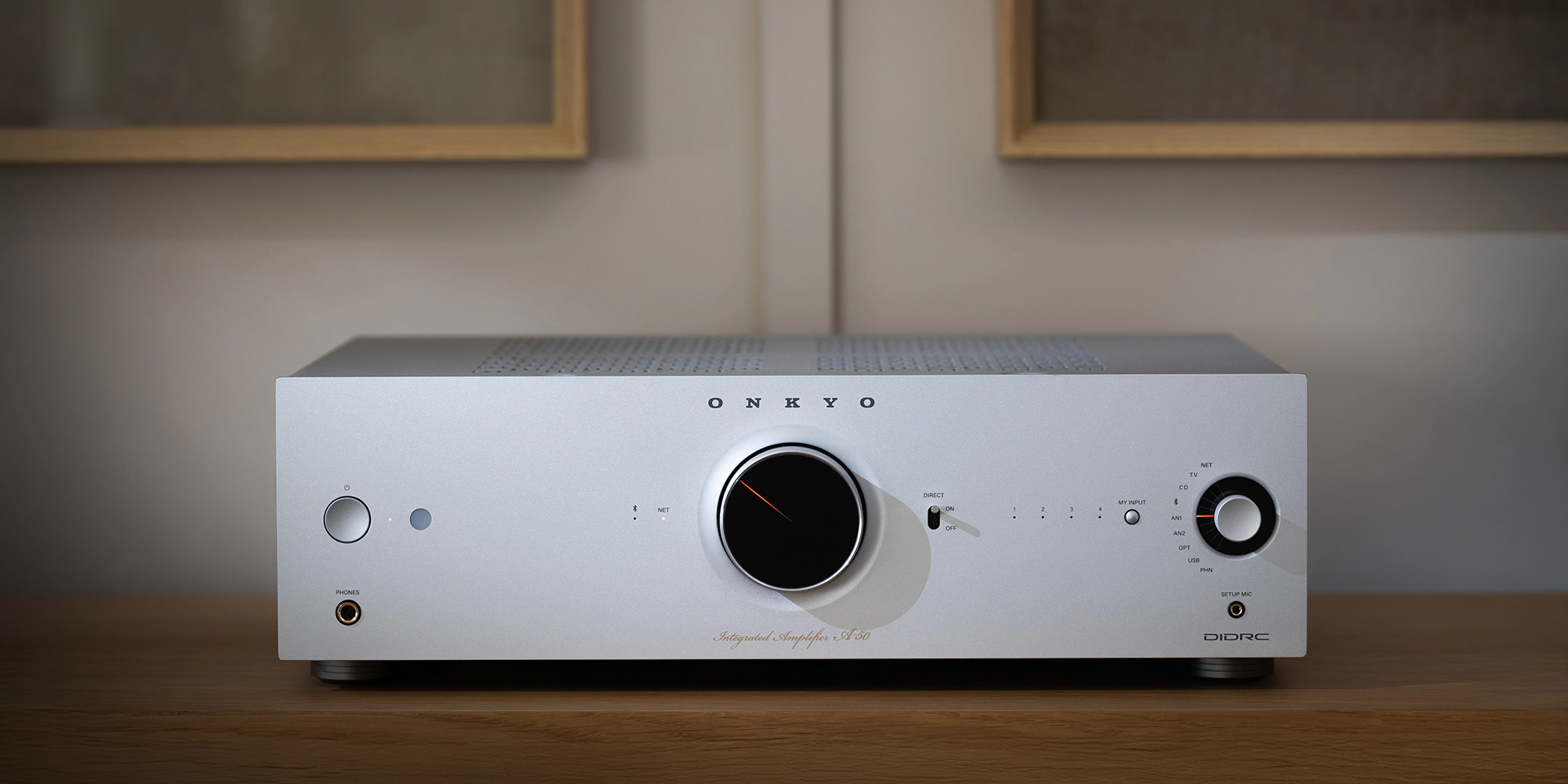 Silver Onkyo Icon A-50 integrated amplifier on an oak cabinet, with black volume dial and orange indicator